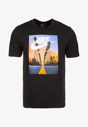 T-shirt noir Nike avec une scène de route au coucher du soleil, comprenant de grands palmiers et un grand logo blanc Nike dans le ciel.