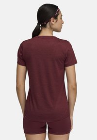 Maroon athletic t-shirt with short sleeves and a rounded hem. Soft, textured fabric, worn with matching shorts. Hair tied back with a band.