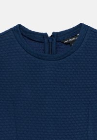 Ένδυμα σε ναυτικό μπλε με υφή, στρογγυλή λαιμόκοψη και φερμουάρ στην πλάτη. Διαθέτει διακριτικό υφασμάτινο μοτίβο για επιπλέον λεπτομέρεια.