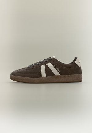 Brauner Wildleder-Sneaker mit weißen Streifen, weißem Fersen-Patch, Gummisohle und dem Text "JACK & JONES" an der Seite, im Profil auf einfarbigem Hintergrund gezeigt.