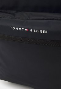 Zaino nero Tommy Hilfiger realizzato in nylon texturizzato. Presenta un logo con accenti rossi e bianchi e un design morbido e strutturato.