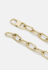 Cadena de metal dorado con eslabones ovalados alargados, un cierre de resorte con grabado "FOSSIL", superficie lisa y acabado brillante.