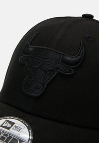 Melnā beisbola cepure ar reljefa bulls logotipu priekšpusē, izgatavota no gludas auduma ar strukturētu dizainu un izliekto malu.