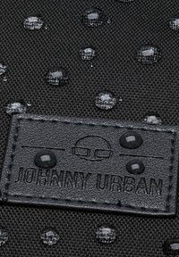 Čierna nepremokavá látka s vyvýšenými kvapkami a textúrovaným povrchom, s čiernou koženou visačkou s embosovaným nápisom "JOHNNY URBAN."