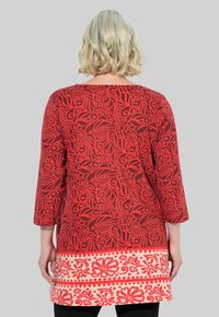 Rood tuniek met bloemenpatroon en driekwartmouwen, met een contrasterende crème rand met decoratieve motieven aan de zoom.