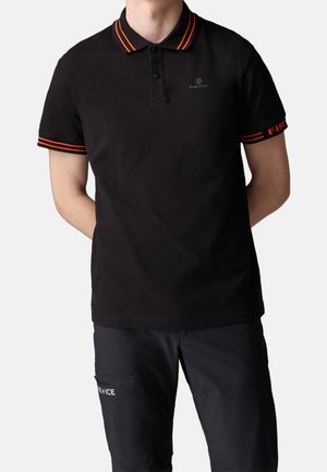 Hombre vistiendo una camisa tipo polo de manga corta negra con rayas naranjas en el cuello y las mangas, combinada con pantalones negros con bolsillo con cremallera y texto "FIRE+ICE".