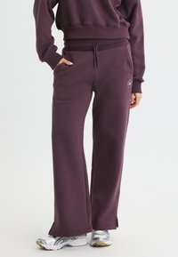 Plommonfärgade sweatpants i mjuk bomullsblandning, med avslappnad passform, sidofickor och delade fållar. Litet logotypdetalj nära fickan.