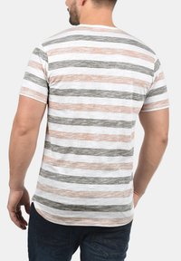 Camiseta a rayas con líneas horizontales en gris, blanco y naranja claro. Manga corta y cuello redondeado, fabricada en tejido suave.
