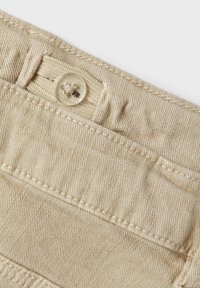 Vaalean beige denim-kangas, jossa on teksturoitu pinta, napituskinnitys ja ommeltu taskutieto. Minimalistinen muotoilu, jossa on puhtaat linjat.
