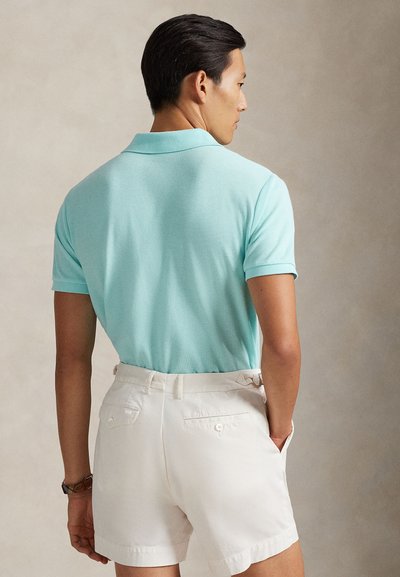 Ανοιχτό γαλάζιο πόλο μπλουζάκι με απαλή υφή, κοντά μανίκια και γιακά. Συνδυάζεται με λευκές βερμούδες που έχουν τσέπες στο πίσω μέρος και θηλιές για ζώνη.