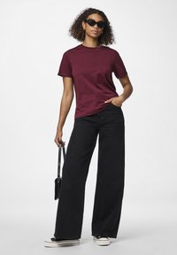 Burgunder crew-neck t-skjorte, avslappet passform, kombinert med høyt liv svarte vide jeans og svarte joggesko. Tilbehøret inkluderer en liten svart veske.