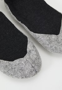 Pantuflas suaves en tonos gris y negro con diseño de punta redonda; la parte superior presenta una textura de punto oscura, mientras que la suela está hecha de fieltro suave.