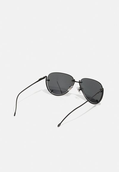Lunettes de soleil noires en métal avec des verres gris, forme œil de chat, design minimaliste, branches fines et accents matériels subtils au niveau des charnières.