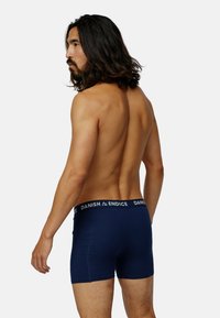 Marinblå kalsonger i bomull med en vit logoband, åtsittande design och mjuk textur. Utsikt från baksidan.