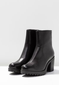 Stivali alla caviglia in pelle nera con un design elegante, punta rotonda e un tacco alto chunky. Presentano una zip laterale e una suola in gomma texturizzata.