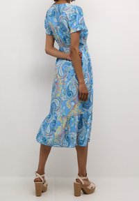 Sininen paisley-kuosiset mekko, jossa on lyhyet hihat, smockattu vyötärö ja frillahelma. Yhdistelty vaaleanvärisiin platform-sandaaleihin.