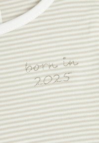 Gestreifter Stoff in einem hellbeige-weißen Farbschema, mit gesticktem Text "geboren 2025" in der Nähe des Ausschnitts. Weiche Textur.