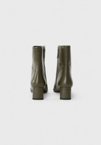 Stivaletti alla caviglia verde oliva con finitura lucida, tacco a blocco e zip laterali per facilitarne l'uso. Tessuto morbido con un design elegante.