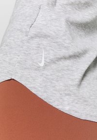 Tessuto grigio a righe con una sezione liscia di colore ruggine nella parte inferiore. Presenta un logo Nike bianco sull'area grigia.