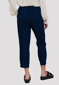 Marineblauwe cropped pants met een elastische tailleband en zijzakken, gemaakt van zachte, gestructureerde stof, gecombineerd met zwarte plateausandalen.