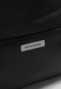 Borsa Moleskine nera con superficie texture e etichetta grigia. Design semplice, senza hardware o dettagli visibili.