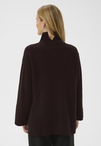 Pull en maille côtelée bordeaux avec col montant, manches longues et taille ajustée. Tissu texturé avec une coupe décontractée.