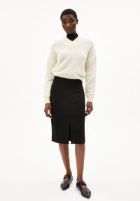 Crème kleurige, fuzzy trui met V-hals gecombineerd met een nauwsluitende zwarte kokerrok met een voorste split. Model draagt zwarte flats met gespsnitsen.