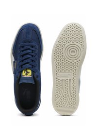 Blå ruskinds sneakers med en hvid gummisål, kontrastsyts, og et gult logo-patch med en springende hest.