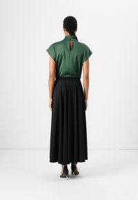 Haut vert à manches courtes avec un détail en forme de trou de serrure à l'arrière, associé à une longue jupe noire à taille élastique. Tissu lisse, silhouette fluide.