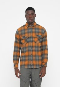 Camisa de franela en un patrón de cuadros naranja y gris, con un diseño de botones, dos bolsillos en el pecho y un dobladillo curvado. Confeccionada en tejido texturizado.