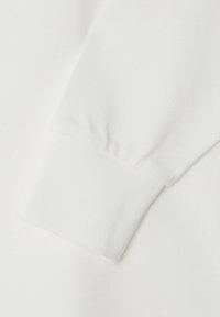 Witte, lange mouwen shirtdetail met textuurstof; heeft een aansluitende polsmanchet en gladde, platte naden voor een nette afwerking.