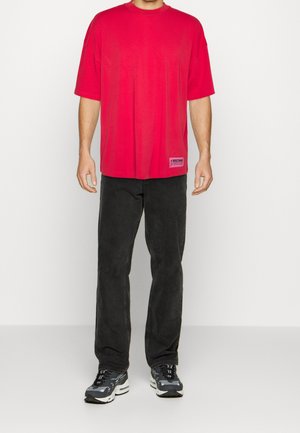 T-shirt rossa oversize con maniche corte, in cotone, con un piccolo logo ricamato. Abbinato a jeans neri e sneakers grigie chunky.