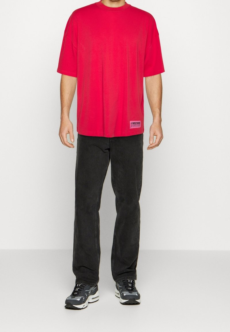 Rotes, übergroßes T-Shirt mit kurzen Ärmeln aus Baumwollmaterial, mit einem kleinen Logo-Patch. Kombiniert mit schwarzen Jeans und kräftigen grauen Sneakers.