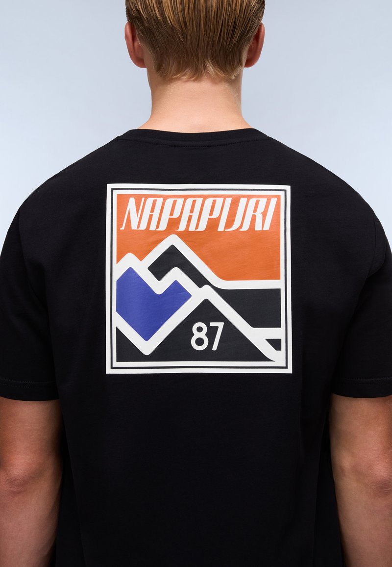 T-shirt nera a maniche corte con una grande grafica rettangolare sulla schiena che presenta la scritta "NAPAPIJRI", montagne e il numero "87" nei colori arancione, blu e bianco.