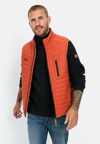 Orangenes gesteppte Weste mit einem Reißverschluss vorne, kombiniert mit einem schwarzen gerippten Pullover. Verfügt über ein dezentes Logo und Reißverschlusstaschen.