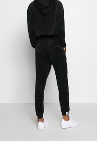 Czarna welurowa crop hoodie z kapturem, w zestawie z dopasowanymi spodniami dresowymi z tylną kieszenią i ściągaczami. Całość dopełniają białe sneakersy.