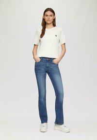 Biała bawełniana koszulka z małym niebieskim sercem, zestawiona z niebieskimi dżinsami o prostym kroju i białymi trampkami. Prosty, casualowy strój.