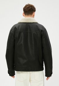 Zwarte leren jas met een zachte, crème-kleurige schapenvacht kraag. Beschikt over een ontspannen pasvorm en zichtbare stikseldetails op de achterkant.