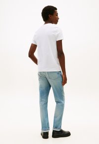 Wit katoenen T-shirt met een ronde hals, gecombineerd met lichtblauwe denim jeans met een rechte snit en subtiele stikseldetails. Zwarte schoenen.