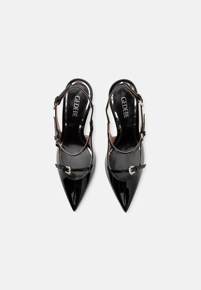 Zapatos de charol negro tipo slingback con punta afilada, detalles plateados y correas ajustables. Textura suave con un acabado brillante.