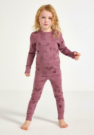 Lille barn med langt, krøllet hår står barfodet iført matchende lilla pyjamas med dyre- og naturmønstre.