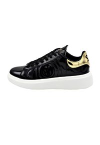 Sneaker in pelle verniciata nera con punta rotonda, dettagli dorati sul tallone, suola bianca spessa e logo circolare testurizzato in nero sul lato.