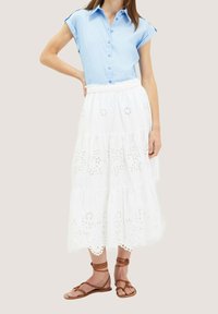 Camicia azzurro chiaro con maniche a risvolto, abbinata a una gonna midi bianca a strati con ricami floreali e sandali marroni con cinturini.