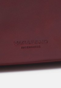 Cuir bordeaux avec une texture lisse, arborant un marquage en relief "VAGABOND" et "SHOEMAKERS". Détails de design élégants et minimalistes.