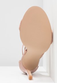 Sandale à talons hauts nu avec une finition brillante, un fin talon aiguille et des bandes texturées. La semelle présente un design de grip nervuré.