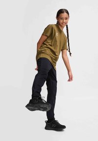 Olivegrünes T-Shirt, kurze Ärmel, entspannte Passform; kombiniert mit navyfarbenen Hosen und schwarzen Sportschuhen mit strukturierten Sohlen und Akzenten.