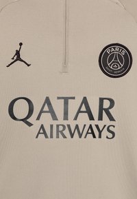 Jersey color crema con diseño de media cremallera. Logo negro de Jordan y parche del PSG en el lado izquierdo del pecho. Texto grande impreso: "QATAR AIRWAYS."