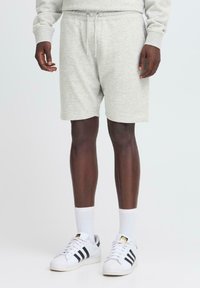 Pantalones cortos de algodón gris claro con cinturilla elástica y cordón, con un ajuste casual. Combinados con zapatillas Adidas blancas y calcetines.