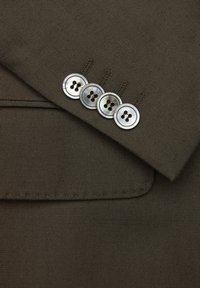 Detalj av mörkbrun tygblazer med en elegant krage och fyra runda, glänsande silverknappar med fyra hål vardera.