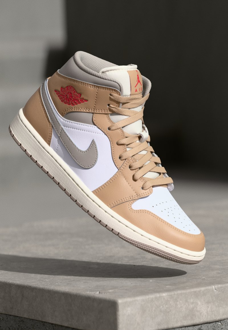Sneaker alta tan e bianca con accenti grigi e logo Air Jordan. Presenta pelle liscia, punta perforata e lacci a contrasto.